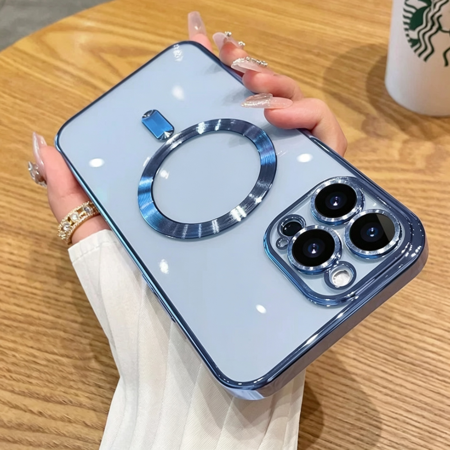 Transparente iPhone-Hülle in Hellblau, Rückansicht in Hand, blau gebürsteter Magnet-Ring und Dreifach-Kameraschutz mit Metall