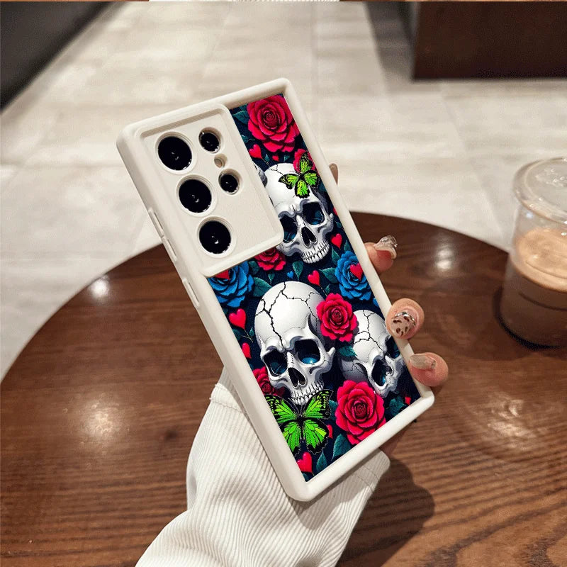 Hand hält weiße Samsung-Hülle mit drei weißen Totenköpfen, roten und blauen Rosen sowie grünen Schmetterlingen