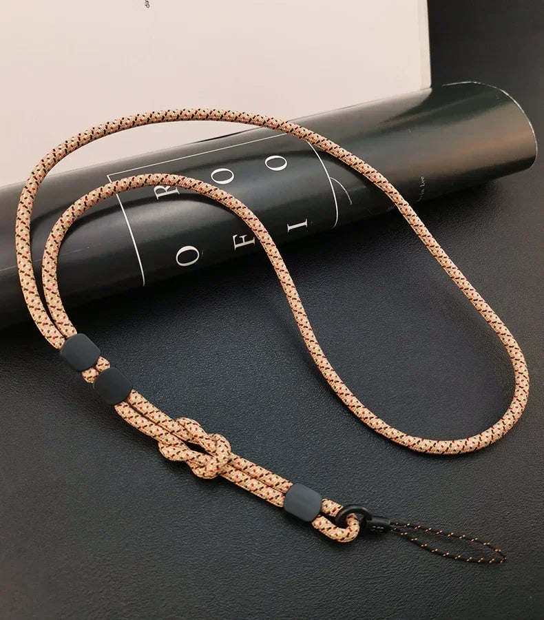 Einzelnes beige-braun gemustertes Handy-Nackenband mit schwarzen Schiebereglern und Knoten, auf schwarzer Fläche neben Magazi