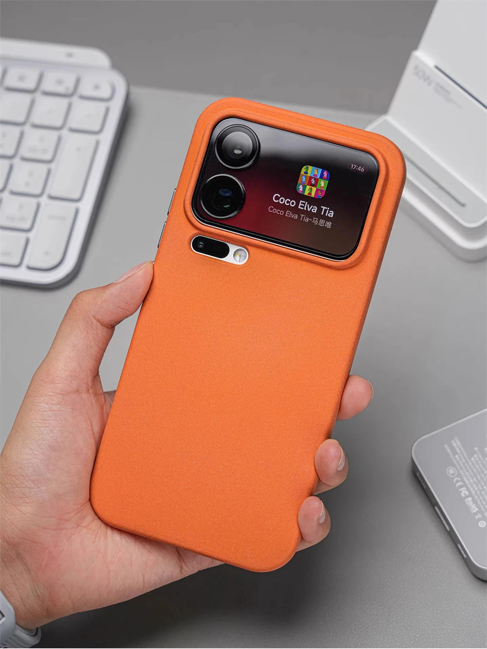 Hand hält Smartphone in orangefarbener matter Silikonhülle, Rückseite mit aktivem Kamera-Außendisplay