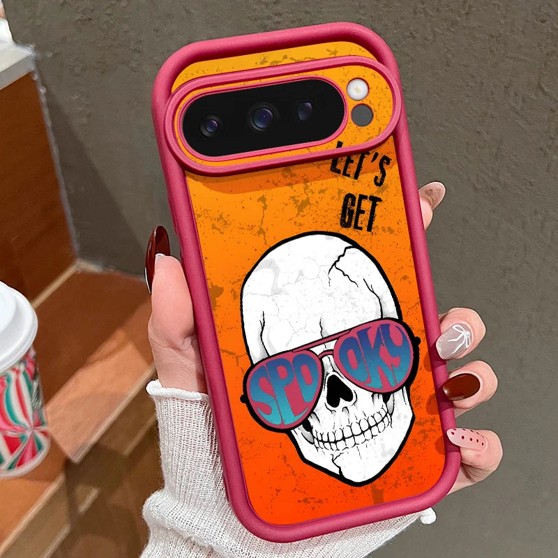 Hand hält orangefarbene Google Pixel Hülle mit Schädel in Sonnenbrille und Aufschrift 'Let's Get Spooky', pink-roter Rahmen