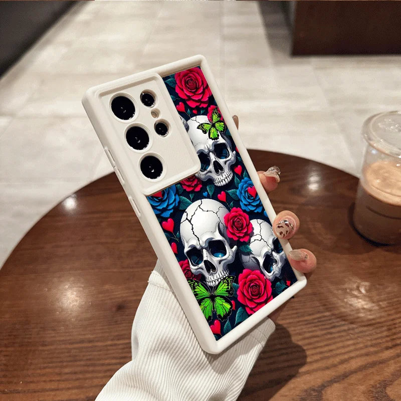 Hand hält weiße Samsung-Hülle mit drei weißen Totenköpfen, roten Rosen, Herzen und grünen Schmetterlingen