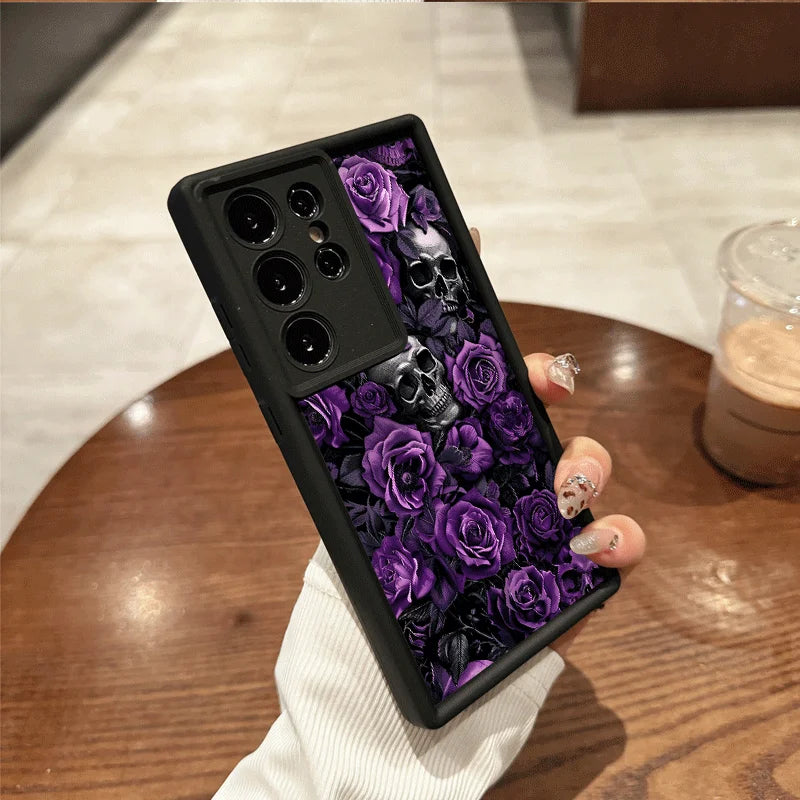 Hand hält schwarze Samsung-Hülle mit lila Rosen und silbergrauen Totenköpfen, Rückansicht auf Holztisch