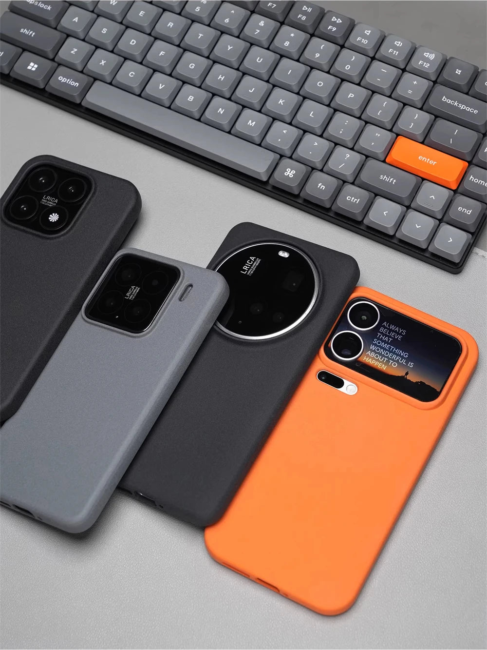 Drei matte Silikonhüllen in Grau, Schwarz und Orange auf grauem Untergrund, verschiedene Smartphonemodelle