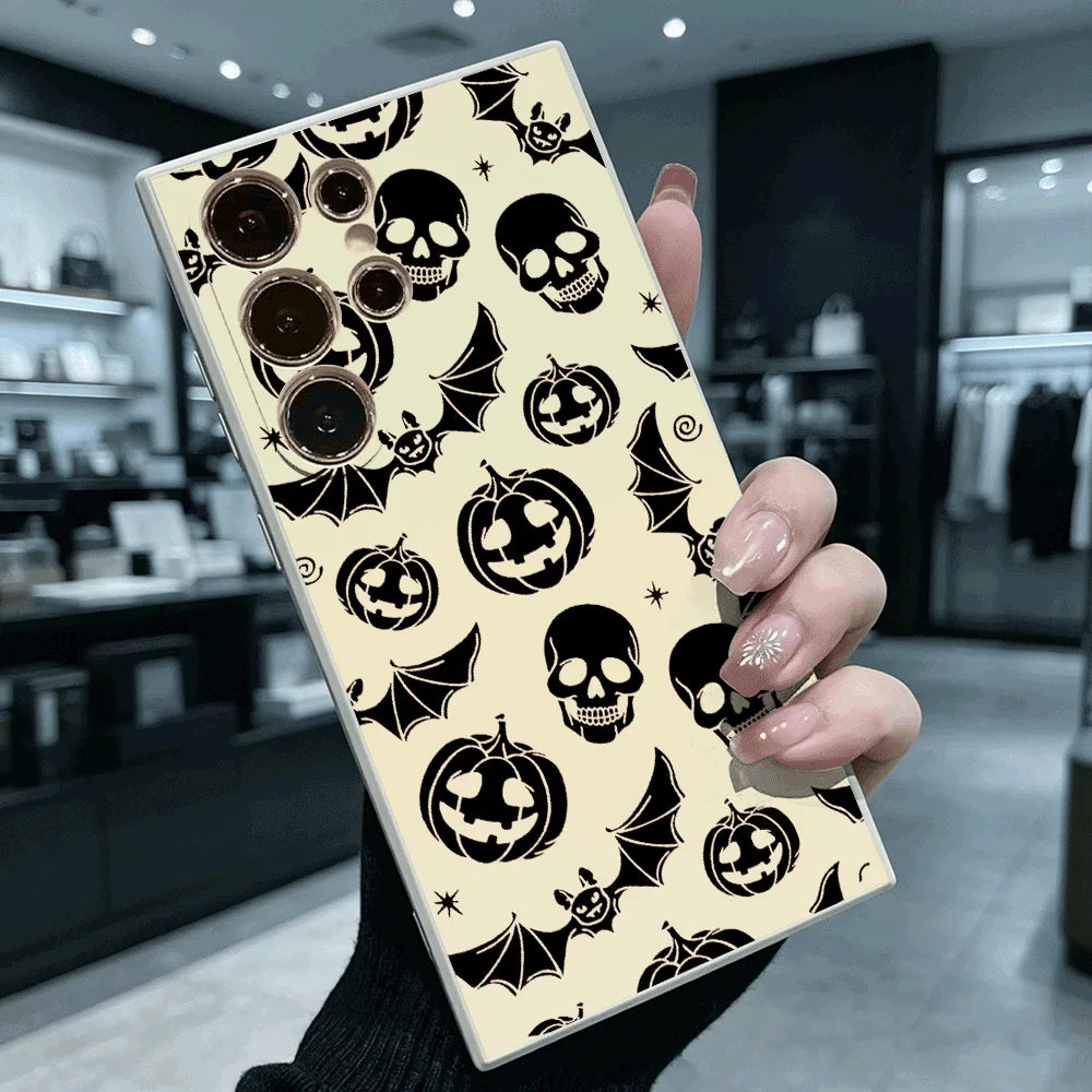 Hand hält cremefarbene Samsung-Hülle mit schwarzem Halloween-Muster aus Totenköpfen, Kürbissen und Fledermäusen, Rückansicht