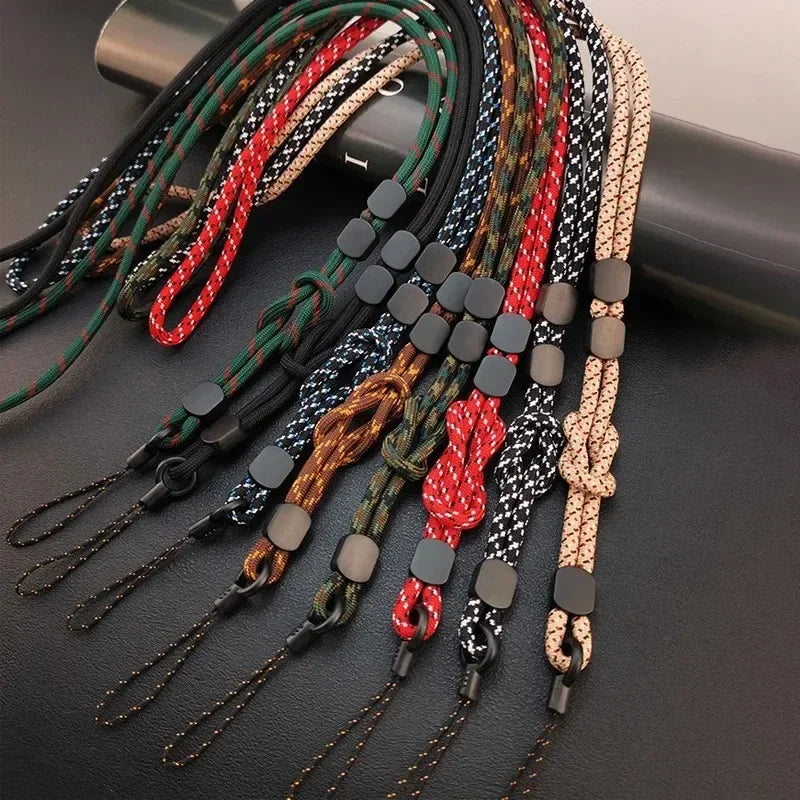 Mehrere geflochtene Handy-Lanyards in Farben wie Schwarz, Rot, Grün, Camouflage und Beige auf dunkler Unterlage