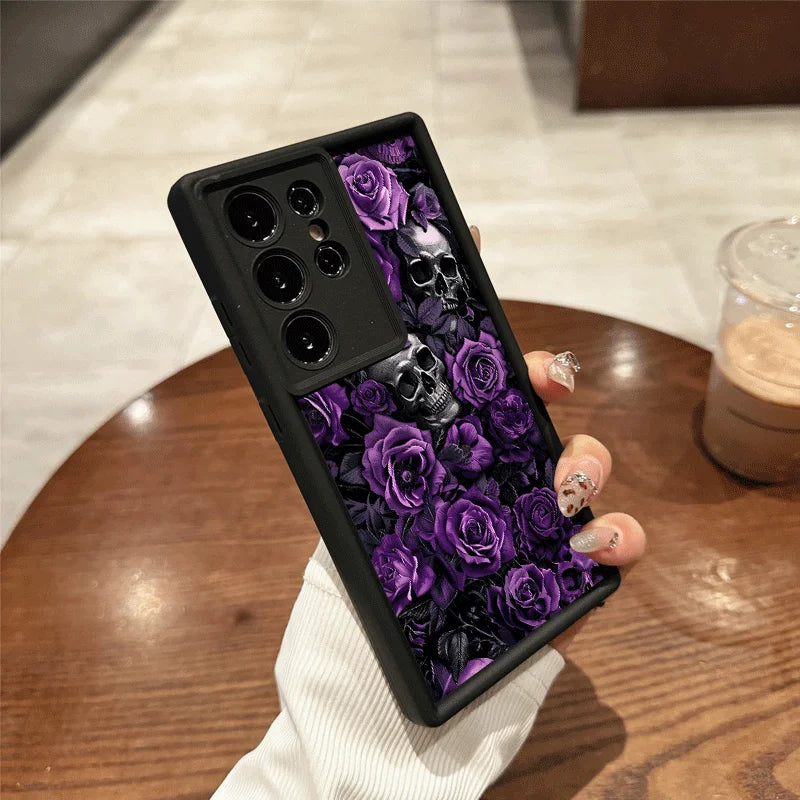 Hand hält schwarze Samsung-Hülle mit lila Rosen und silbernen Totenköpfen, Rückansicht auf Holztisch
