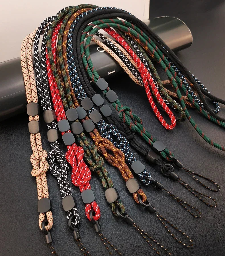 Sieben geflochtene Handy-Lanyards in Beige, Rot, Schwarz, Camouflage und Dunkelgrün auf schwarzer Unterlage, Draufsicht