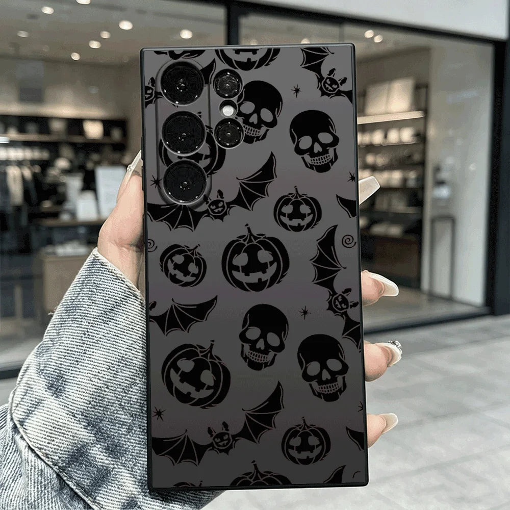 Hand hält schwarze Samsung-Hülle mit dunklem Halloween-Allover-Muster aus Totenköpfen, Kürbissen und Fledermäusen